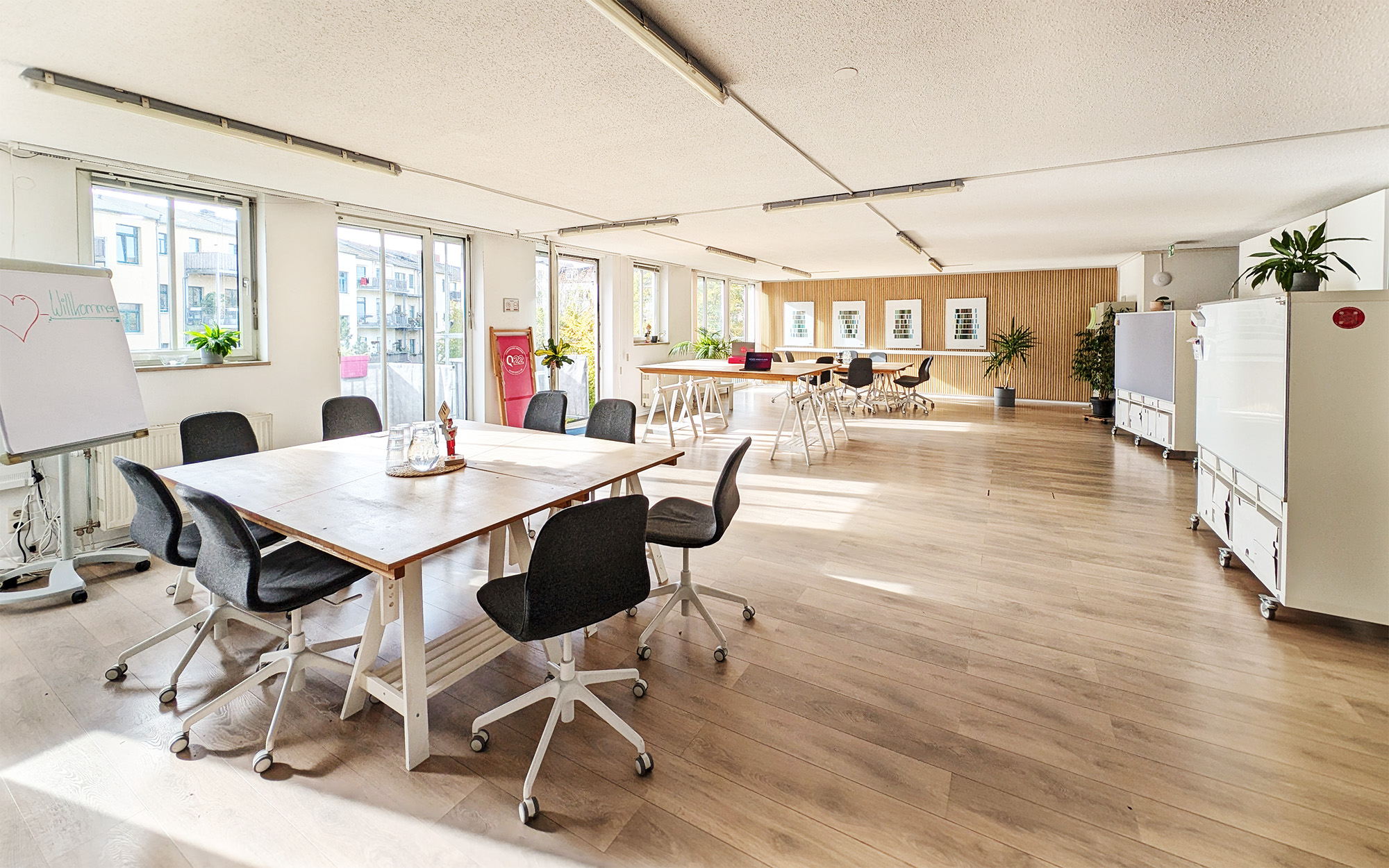 Eventraum mieten Dresden Neustadt Mohalla: Großer Raum mit langen Tischen in Arbeitsinseln, Blick auf den Balkon.