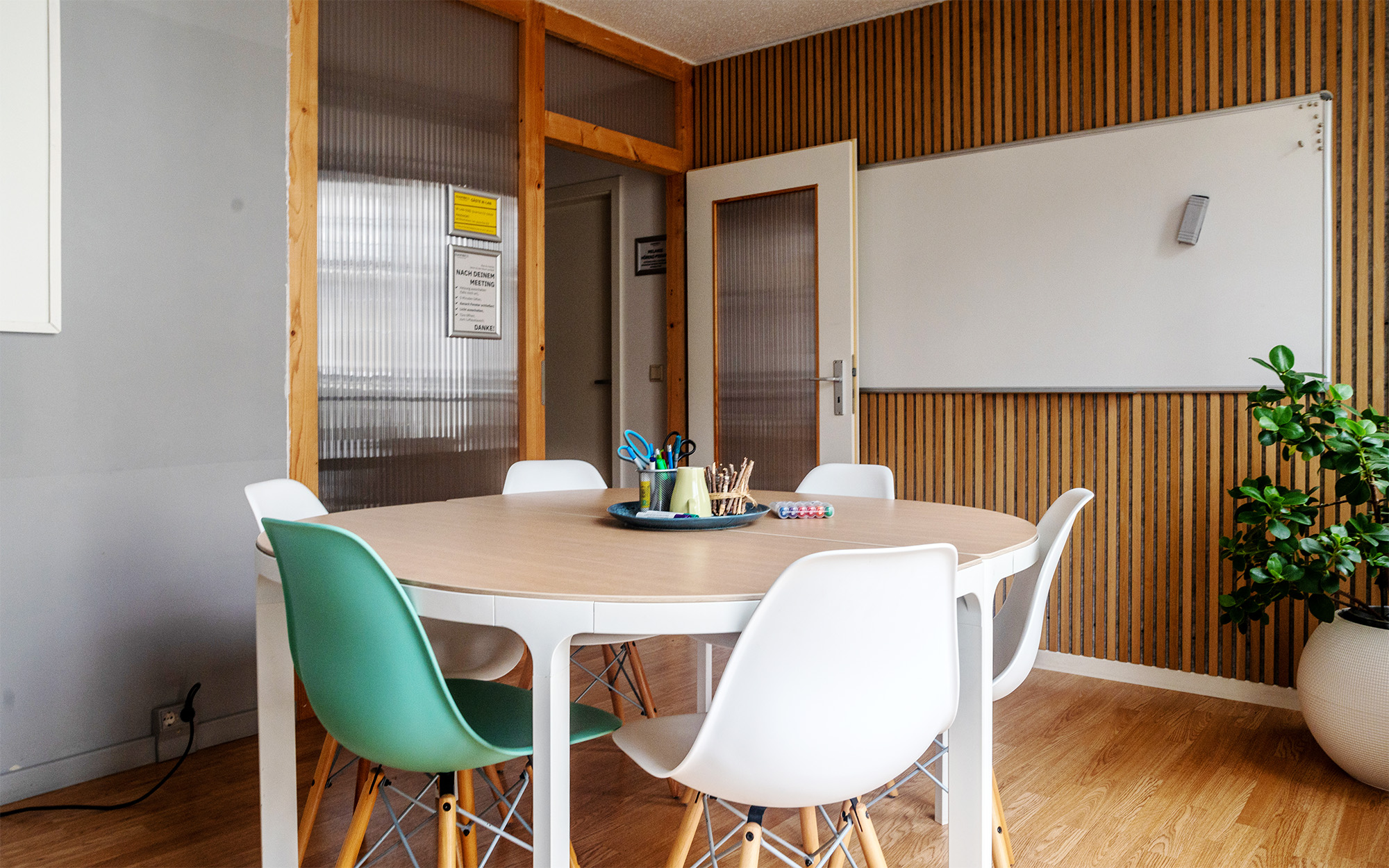 Meetingraum mieten Dresden Neustadt: Runder Besprechungstisch, bunte Stühle, Whiteboard, Holzwand.